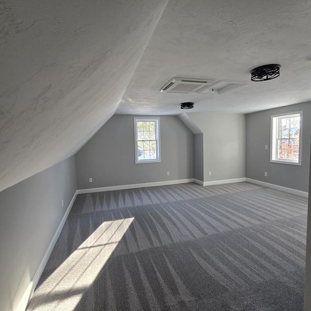 bonus room featuring lofted ceiling, a textured ceiling, and dark colored carpet