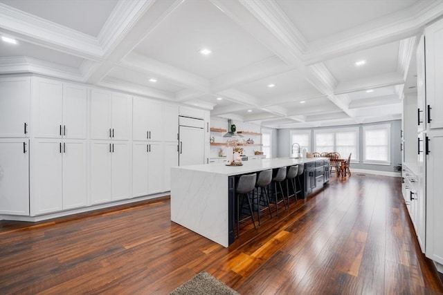 kitchen with a breakfast bar area, a spacious island, paneled built in refrigerator, beam ceiling, and white cabinets