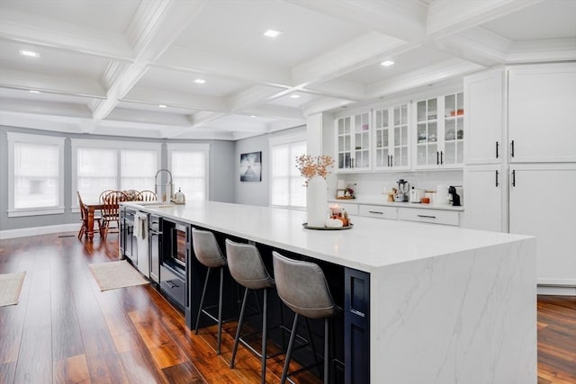 kitchen with a large island with sink, dark hardwood / wood-style floors, beamed ceiling, coffered ceiling, and white cabinets