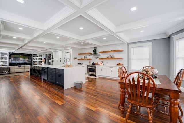 kitchen with beamed ceiling, white cabinetry, stainless steel stove, and an island with sink