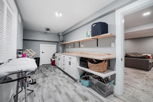 interior space with white cabinets, light wood-type flooring, wooden counters, and sink