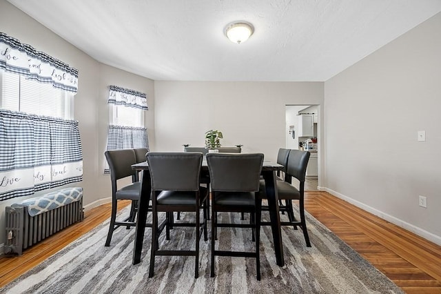 dining space with wood finished floors, radiator, and baseboards