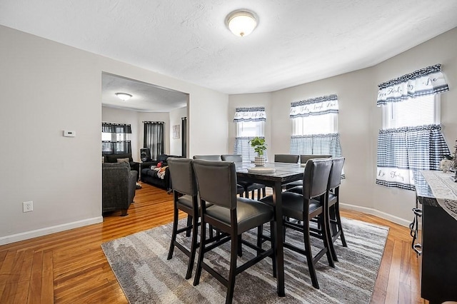 dining area with baseboards, light wood-type flooring, and a textured ceiling