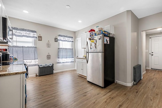 kitchen with freestanding refrigerator, radiator, wood finished floors, white cabinets, and baseboards