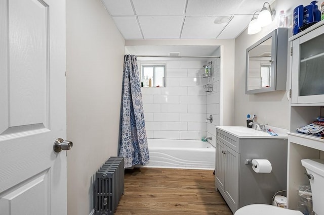 bathroom featuring radiator, toilet, wood finished floors, shower / bathtub combination with curtain, and vanity