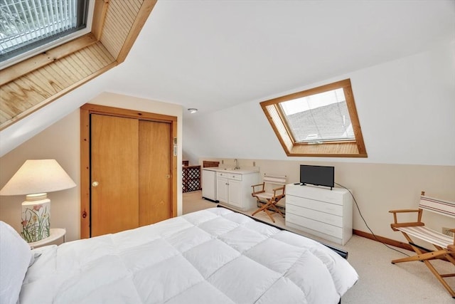 bedroom with a closet, light colored carpet, a sink, baseboards, and lofted ceiling with skylight