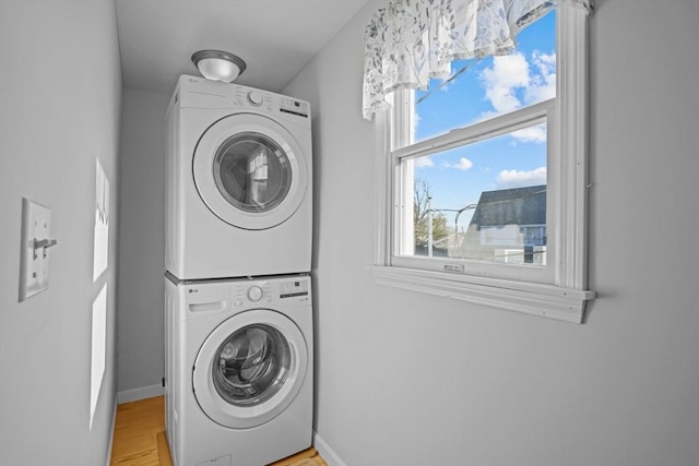 clothes washing area featuring baseboards, light wood finished floors, stacked washer / dryer, and laundry area
