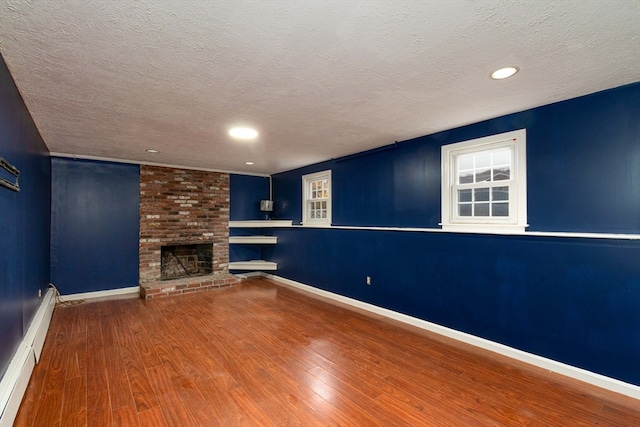 unfurnished living room featuring baseboard heating, a fireplace, hardwood / wood-style floors, and a textured ceiling