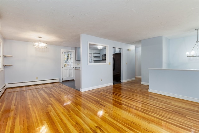 unfurnished living room featuring a textured ceiling, hardwood / wood-style floors, a baseboard heating unit, and an inviting chandelier