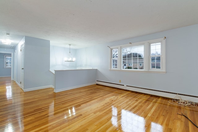 unfurnished room with hardwood / wood-style floors, a baseboard heating unit, and a notable chandelier