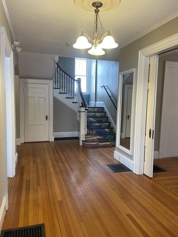 unfurnished living room with hardwood / wood-style floors, ornamental molding, and an inviting chandelier