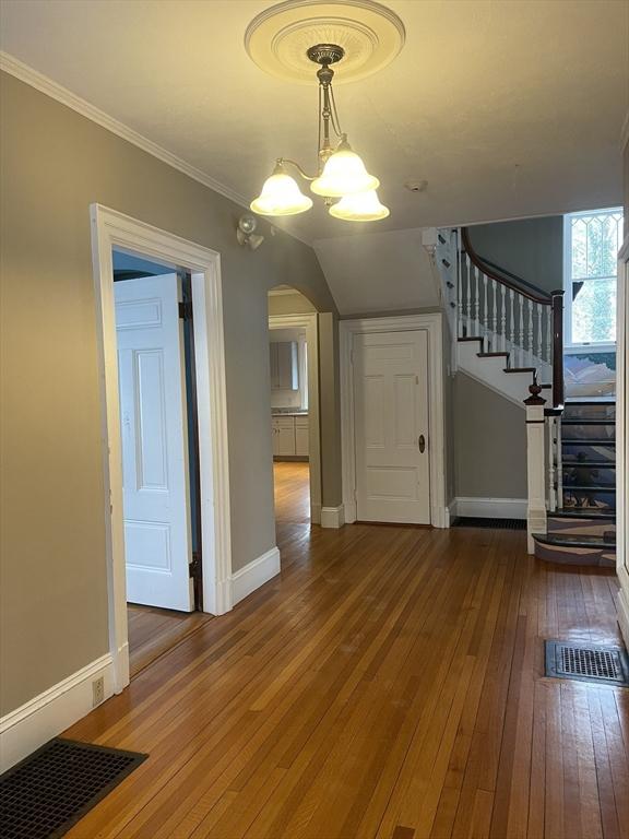 unfurnished living room with hardwood / wood-style flooring, crown molding, and an inviting chandelier