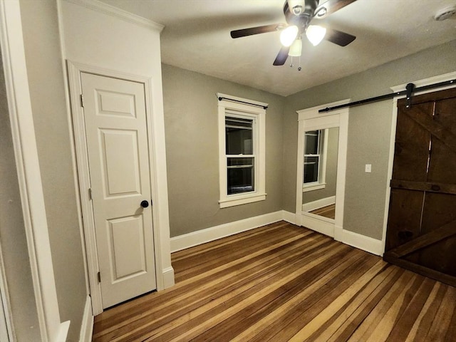 unfurnished bedroom featuring hardwood / wood-style flooring, a barn door, and ceiling fan