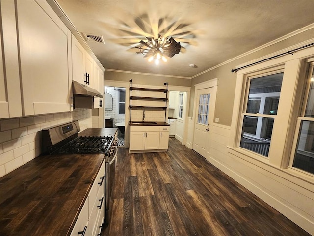 kitchen featuring crown molding, dark wood-type flooring, stainless steel gas range oven, white cabinets, and a barn door