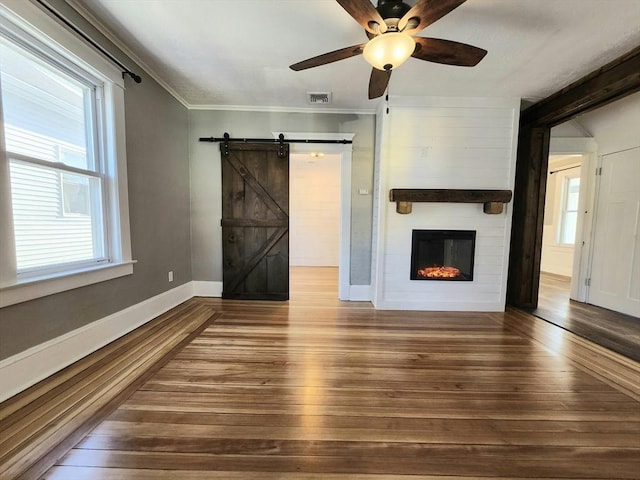 unfurnished living room with a fireplace, hardwood / wood-style flooring, ornamental molding, ceiling fan, and a barn door