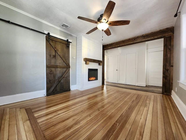 unfurnished living room with wood-type flooring, a barn door, ceiling fan, and a fireplace