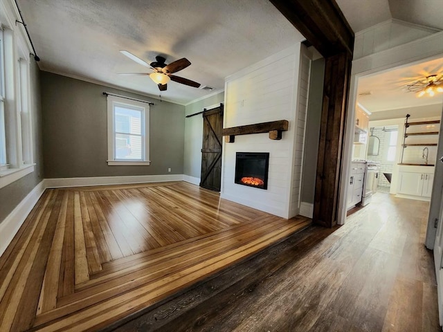 unfurnished living room featuring hardwood / wood-style flooring, ornamental molding, a barn door, and ceiling fan