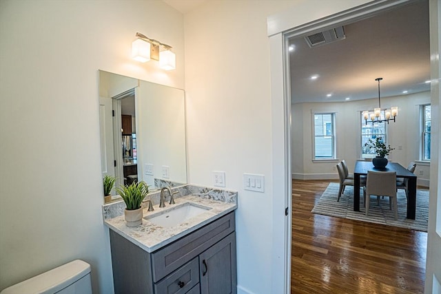 half bathroom featuring visible vents, vanity, wood finished floors, toilet, and a chandelier