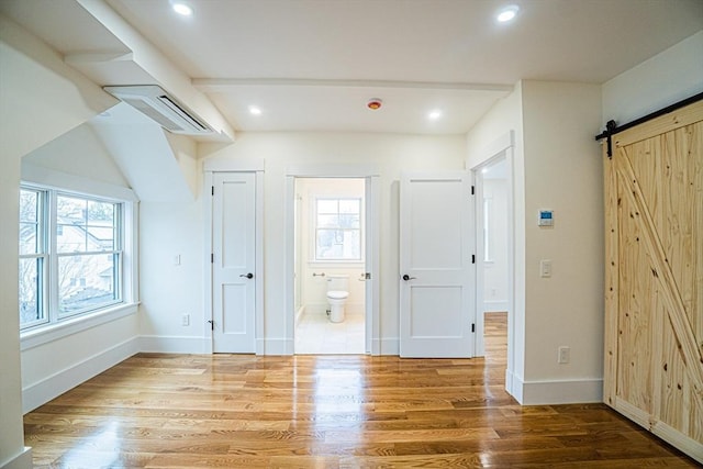additional living space featuring baseboards, plenty of natural light, a barn door, and wood finished floors