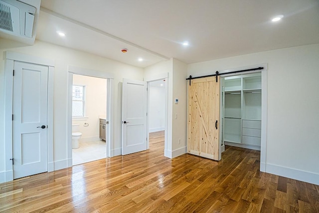 unfurnished bedroom with a walk in closet, baseboards, a barn door, and wood finished floors