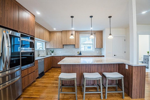 kitchen with a sink, appliances with stainless steel finishes, tasteful backsplash, and wood finished floors