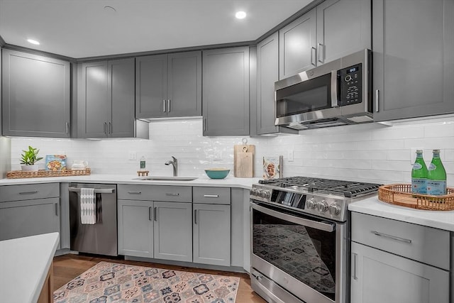 kitchen with stainless steel appliances, light countertops, gray cabinetry, and a sink