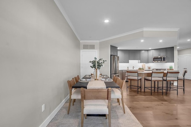 dining space with light wood-style floors, baseboards, ornamental molding, visible vents, and recessed lighting
