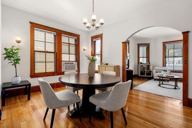dining room featuring light wood-style floors, arched walkways, cooling unit, and an inviting chandelier
