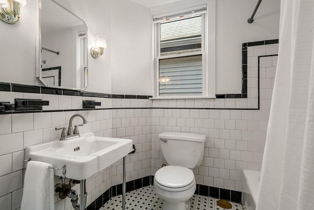 bathroom with tile walls, a sink, a wainscoted wall, toilet, and shower / tub combo with curtain