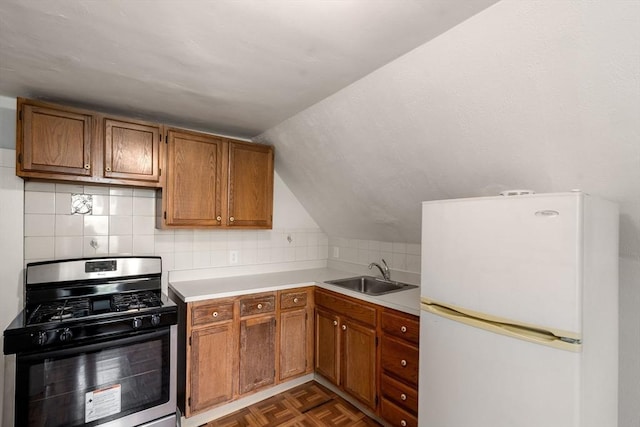 kitchen with a sink, stainless steel range with gas stovetop, light countertops, brown cabinetry, and freestanding refrigerator