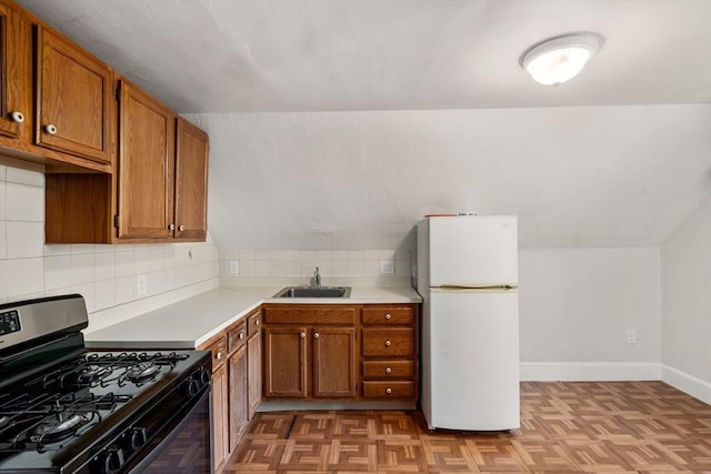 kitchen with a sink, brown cabinets, freestanding refrigerator, and stainless steel range with gas cooktop