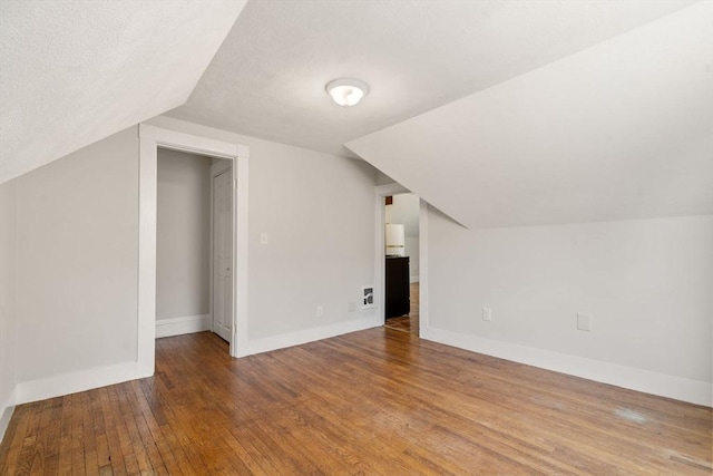 additional living space with a textured ceiling, hardwood / wood-style floors, baseboards, lofted ceiling, and visible vents
