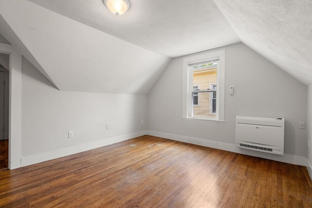additional living space with a textured ceiling, hardwood / wood-style floors, baseboards, heating unit, and lofted ceiling