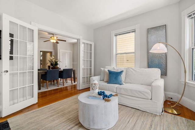 living area featuring baseboards, a ceiling fan, french doors, and wood finished floors