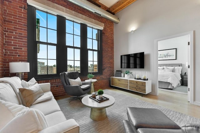 living area featuring a wealth of natural light, light wood-style flooring, a towering ceiling, and brick wall