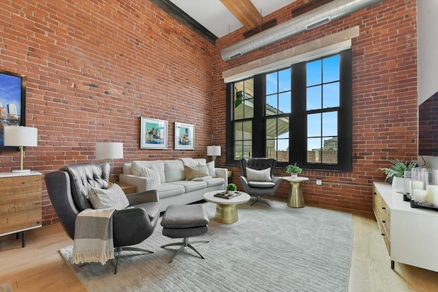 living room featuring brick wall, a high ceiling, and light wood-style floors