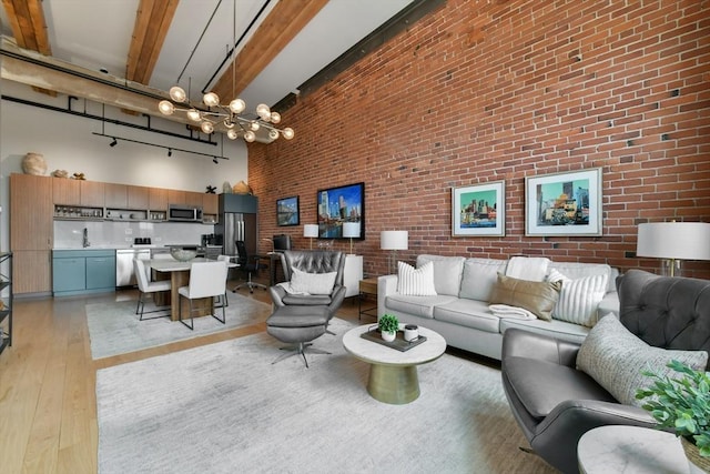 living area featuring a notable chandelier, light wood-type flooring, brick wall, beam ceiling, and a high ceiling