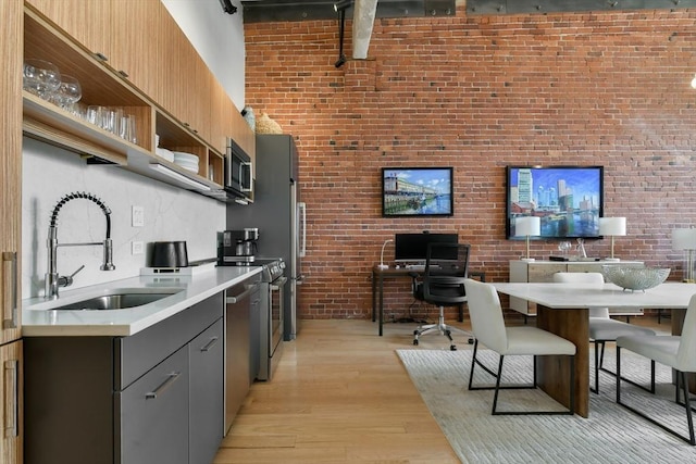 kitchen featuring light wood finished floors, brick wall, a sink, open shelves, and light countertops