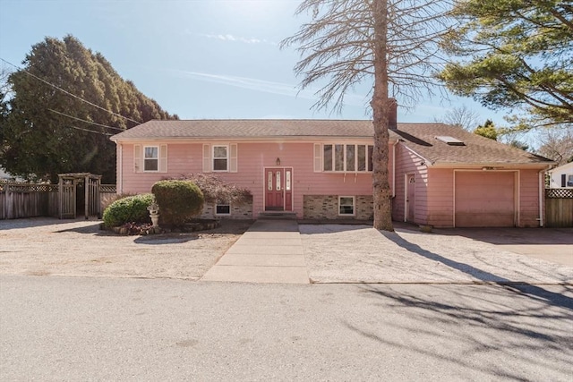 raised ranch with an attached garage, driveway, and fence