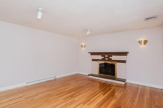 unfurnished living room featuring wood finished floors, baseboards, visible vents, a baseboard radiator, and a brick fireplace