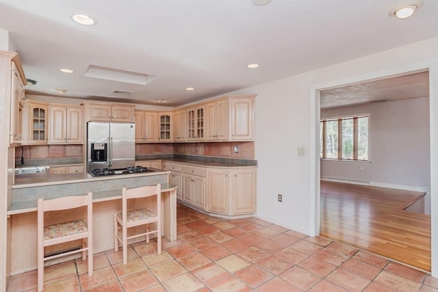 kitchen featuring a sink, glass insert cabinets, a kitchen breakfast bar, and stainless steel refrigerator with ice dispenser