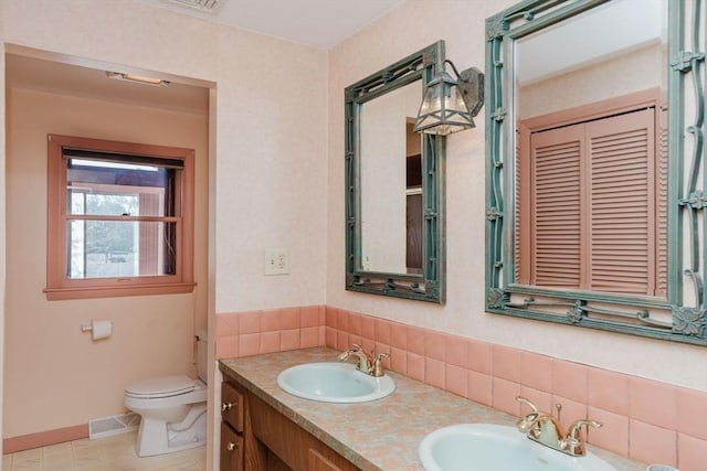 bathroom with double vanity, toilet, baseboards, and a sink