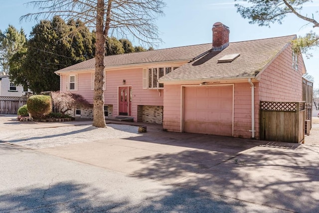 bi-level home with a shingled roof, fence, concrete driveway, a chimney, and a garage