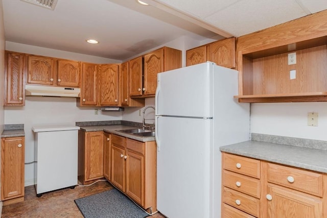 kitchen featuring a sink, under cabinet range hood, brown cabinetry, and freestanding refrigerator