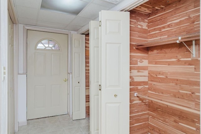 foyer entrance with a paneled ceiling, wooden walls, and light tile patterned flooring