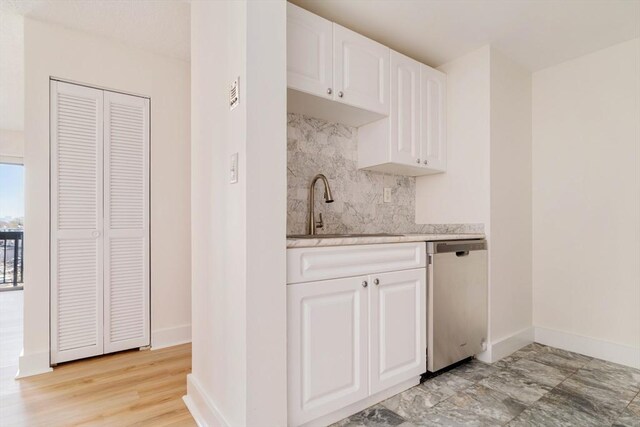 kitchen featuring dishwasher, a sink, baseboards, backsplash, and white cabinets
