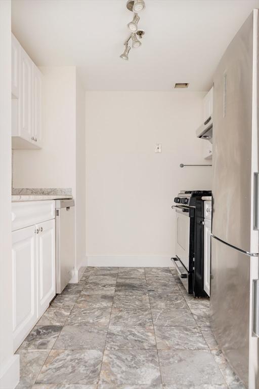 kitchen featuring range with gas cooktop, freestanding refrigerator, light marble finish flooring, white cabinetry, and under cabinet range hood