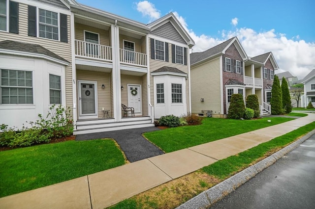 townhome / multi-family property with a balcony, a front lawn, a residential view, and covered porch