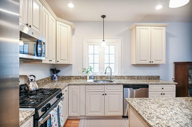 kitchen with stainless steel appliances, a sink, pendant lighting, light stone countertops, and recessed lighting