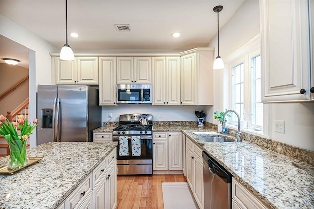 kitchen with appliances with stainless steel finishes, a sink, light wood-type flooring, light stone countertops, and recessed lighting